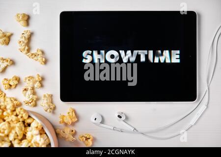 Showtime logo on the tablet screen laying on the white table with scattered popcorn and Apple earphones. Spending free time at home or news Stock Photo