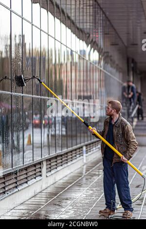 Oxford, UK, 12/09/2009: A caucasian man wearing boots, overalls and a leather jacket is cleaning the exterior windows of a building using a telescopic Stock Photo
