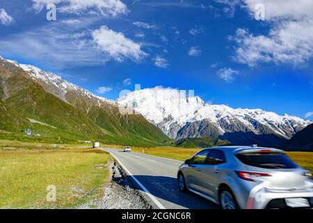 Cars run on highways in the morning with blue skies and clouds in summer. There are green grass beside the roads in Mount Cook National Park, Aoraki, Stock Photo