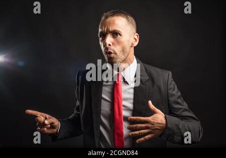 Surprised man in suit pointing to copy space. Black background, Medium shot Stock Photo