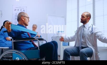Recovery program for invalid senior persons, training with elastic band under doctor supervision in private recovery facility. Invalid physiotherapy program, health care injury rehabilitation in hospital or clinic Stock Photo