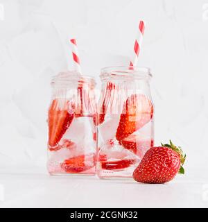 Cold fresh fruit beverage of ripe strawberry with ice, soda water, bubbles, funny striped straw on simple soft bright white background, square. Stock Photo