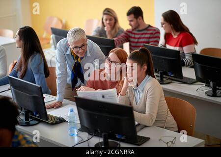 Students asking female professor for help at an informatics lecture in the university computer classroom Stock Photo