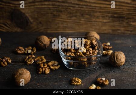 Walnut in a smale plate with scattered shelled nuts and whole nut which standing on a wooden vintage table. Walnuts is a healthy vegetarian protein Stock Photo