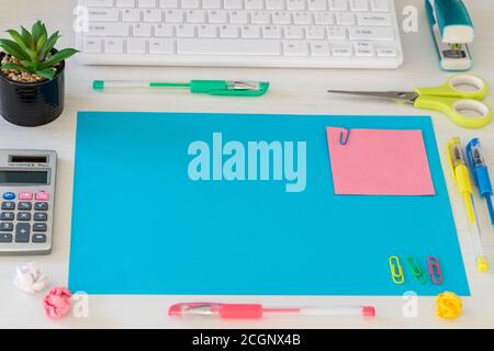 A large, blank blue card on the desk and a small pink card with space for text. Office and school accessories, computer keyboard, calculator, pens, cr Stock Photo