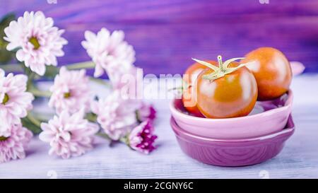 Ripe tomatoes and pink chrysanthemums on purple wooden background, 16 on 9 format Stock Photo