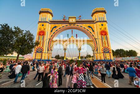 Traditionally dressed Spaniards with flamenco dresses in front of the illuminated Portada, entrance gate, Feria de Abril, Seville, Andalusia, Spain Stock Photo