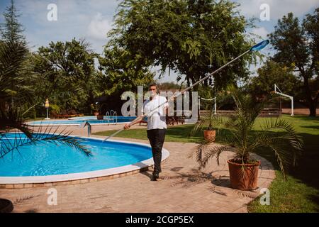 A caucasian gardener with a net for cleaning the pool next to the pool in nature Stock Photo