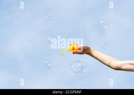 childs hand holding a wand for blowing soap bubbles against the blue sky on a sunny summer day Stock Photo