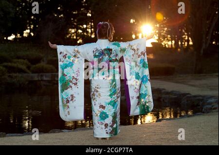 Japanese teenager wearing traditional kimono back and arms outstretched with beautiful flare and sunshine celebrating the Coming of Age Day. Stock Photo