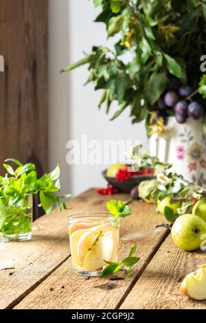 Autumn apple drink, apple slices with juice and mint in a glass on a wooden table, leaves in a vase, morning in the village, rustic concept Stock Photo