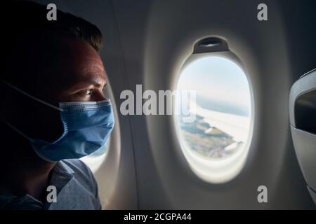 Man wearing face mask inside airplane during flight. Themes new normal, coronavirus and personal protection. Stock Photo