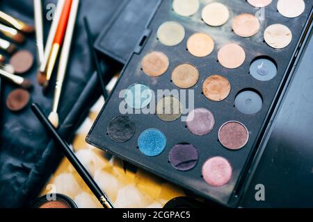 Makeup artist set. Close-up of a palette of eyeshadows of different colors and brushes for applying makeup on a blurred background in a black cosmetic Stock Photo