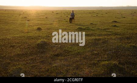 Lonely girl sits on a chair in the middle of the field Stock Photo