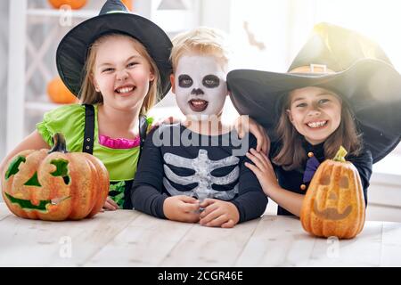 Happy brother and two sisters on Halloween. Funny kids in carnival costumes indoors. Cheerful children play with pumpkins. Stock Photo