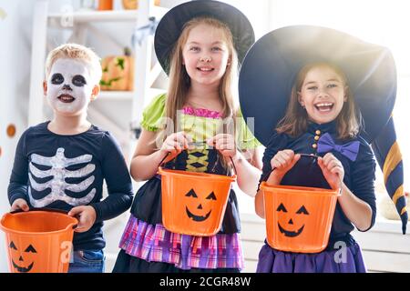 Happy brother and two sisters on Halloween. Funny kids in carnival costumes indoors. Cheerful children play with pumpkins and candy. Stock Photo