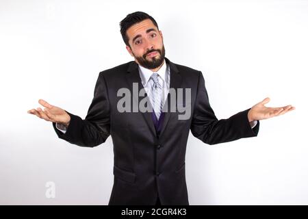 Handsome businessman in suit shrugging shoulders. No idea, don't know concept. Attractive young stylish bearded man doubting and confused. Medium shot Stock Photo