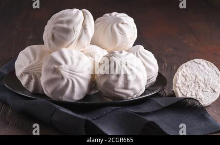 Delicious white marshmallows on a black plate, black napkin, on a wooden background Stock Photo