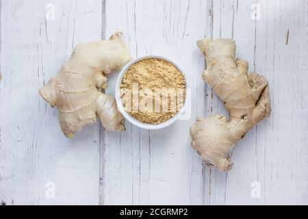 Grounded ginger and ginger root on white wooden surface. Stock Photo