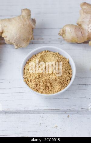 Grounded ginger and ginger root on white wooden surface. Stock Photo