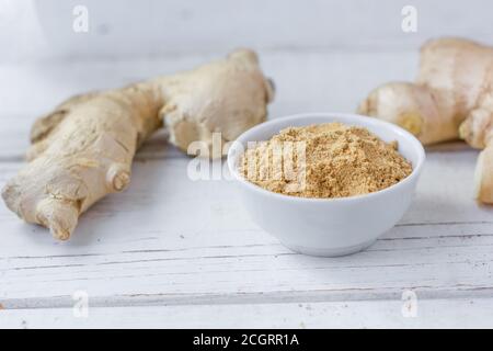 Grounded ginger and ginger root on white wooden surface. Stock Photo