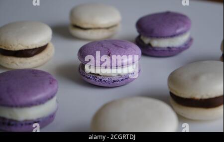 Violet and white almond and meringue macaroons on a white table topped with white and dark chocolate dulce de leche mouse and whipped cream. Stock Photo