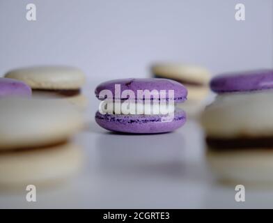 Violet and white almond and meringue macaroons on a white table topped with white and dark chocolate dulce de leche mouse and whipped cream. Stock Photo