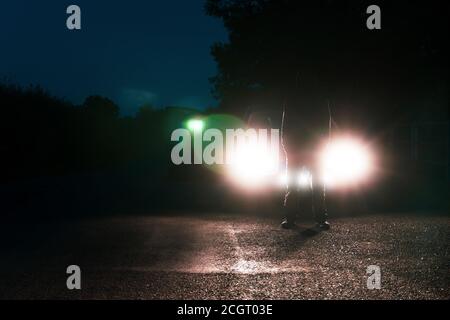 A man in front of a car, standing in the middle of a road, silhouetted against car headlights Stock Photo