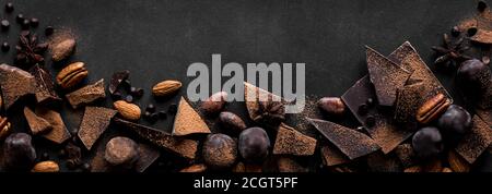 Chocolate and Nuts Background. Chocolate pieces, truffles, cacao powder, nuts and spices on black table, banner, copy space. Stock Photo