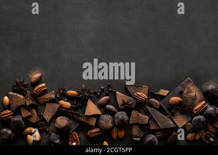 Chocolate and Nuts Background. Chocolate pieces, truffles, cacao powder, nuts and spices on black table, top view, copy space. Stock Photo