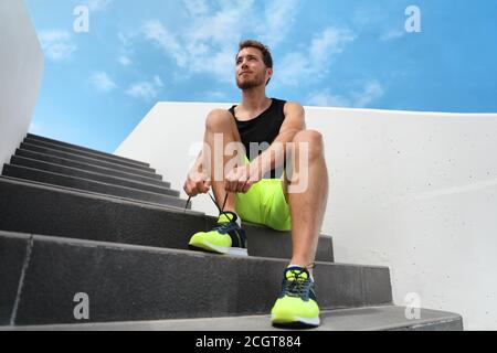 Runner man getting ready to train outdoor on city stairs gym outside tying running shoes laces training cardio workout exercise on staircase. Acitve Stock Photo