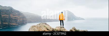 Trail runner man dressed orange waterproof jacket, running tights and shoes enjoying Atlantic ocean bay view on Ponta de Sao Lourenço peninsula -the e Stock Photo
