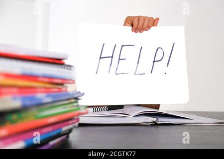 Help! Learning difficulties, school, education concept. Many books on the table and kid hand holding sheet of paper with word Help Stock Photo