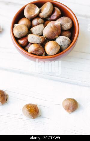 Raw chestnuts in ceramic bowl on white surface. Stock Photo