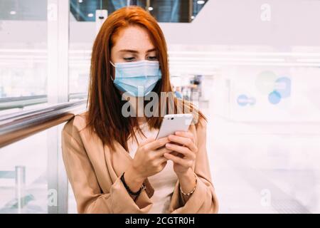 woman with a mask sending a text message using her smartphone at the train station Stock Photo