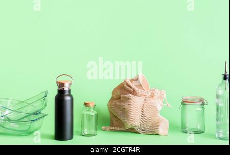 Sustainable lifestyle concept with glass objects, thermos and biodegradable coffee cups, isolated on green background. Plastic-free household products Stock Photo