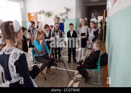 female photographer takes pictures of smart first-graders after the lessons in the school corridor of the municipal rural primary school. Stock Photo