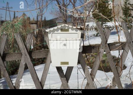 The damaged mailbox, in the form of a house, hangs on a wooden fence in the spring. Stock Photo