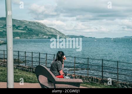 Young woman drinks from disposable mug in front of the sea. Stock Photo