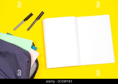 Blue backpack with school supplies and open notebook on yellow background, close up. Top view Stock Photo