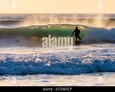 The silhouette of a surfer surfing a wave in Cornwall as the sunsets Stock Photo