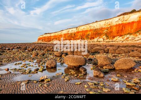 Remains of a wave-cut platform in front of the famous red & white striped cliffs at the east coast seaside town of Hunstanton in Norfolk. Stock Photo