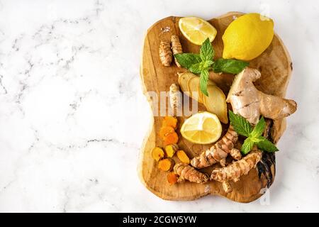 Wooden board with ginger, turmeric roots, lemon and mint seeing from above on white background. Copy space Stock Photo