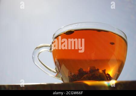 Transparent cup with black flower tea on the table. Background blue sky with sun. Stock Photo