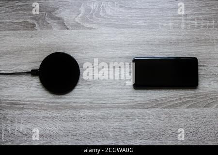 Smartphone next to a wireless charger on a wooden desk Stock Photo