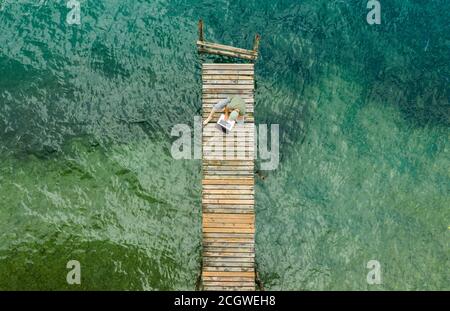Caucasian Men Working on His Laptop While on Vacation. Computer Remote Work on Wooden Pier Aerial View. Stock Photo