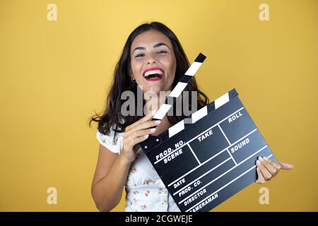 Beautiful woman over yellow background holding clapperboard very happy having fun. Stock Photo