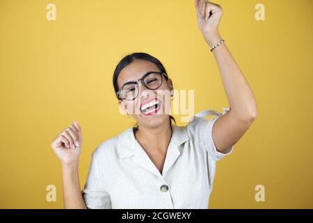 Beautiful woman over yellow background very happy and excited making winner gesture with raised arms, smiling and screaming for success. Stock Photo