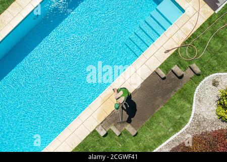 Modern Residential Backyard Garden with Pool New Natural Grass Turfs Installation by Professional Caucasian Landscaper in His 40s. Stock Photo