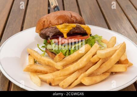 Large and tall cheeseburger topples over from the weight of large patty, melted cheese, sliced tomatoes, and lettuce for a lunch time meal. Stock Photo